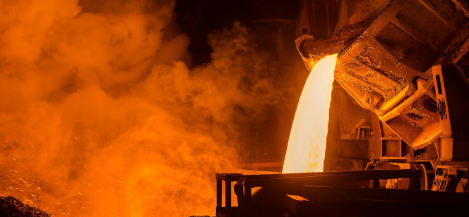 A massive ladle pours bright, molten metal into a container in a foundry, surrounded by orange flames and dark smoke, casting an intense glow across the scene.